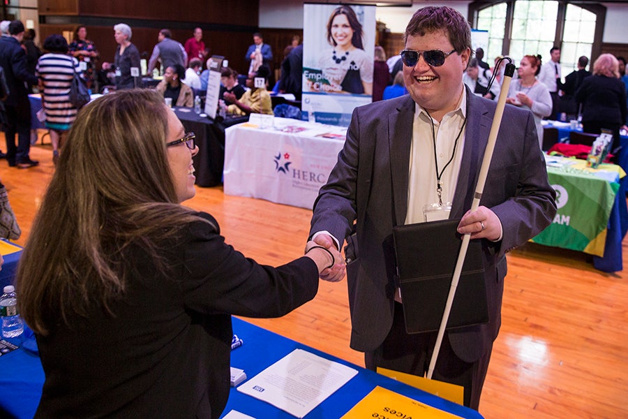 A man wearing sunglasses and holding a white cane shakes hands with a job recruiter