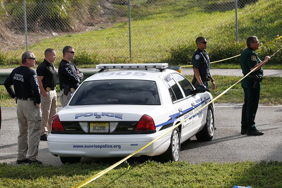 Police officers surround a squad card behind caution tape