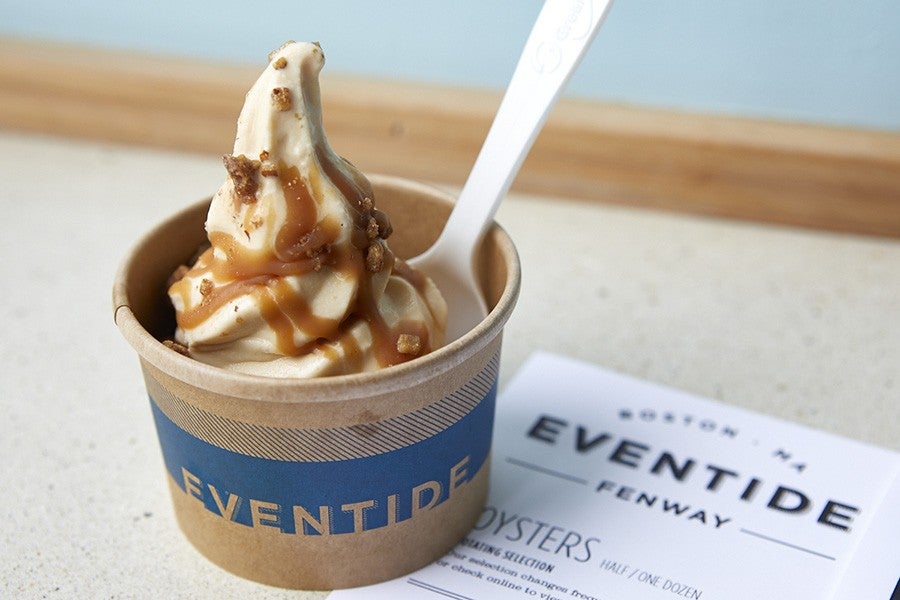 A swirl of soft-serve, drizzled with caramel, is served in a brown paper cup with Eventide branding.