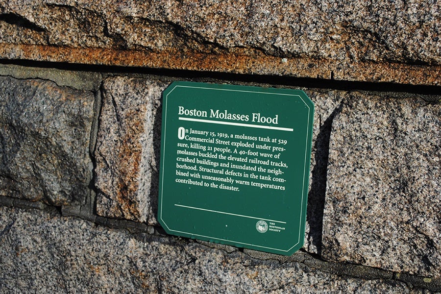 A green historic marker titled 'Boston Molasses Flood' mounted on a rough granite stone wall outdoors.