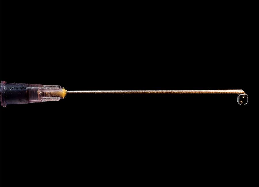 Close-Up Of Syringe Dripping Medicine Against Black Background