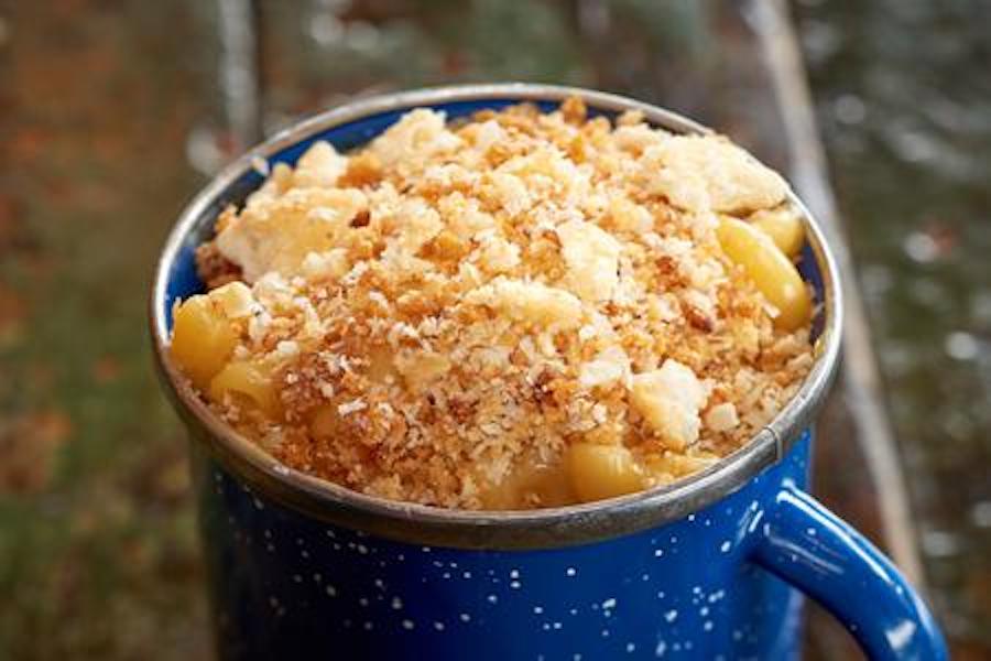 A small blue camping mug is full of mac and cheese topped with Ritz crumbs.