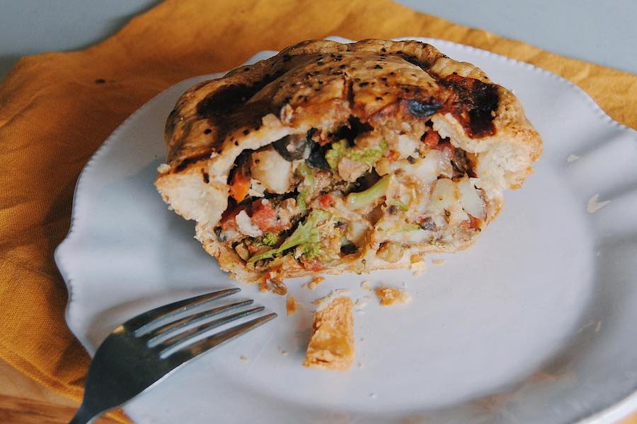 A small round pot pie is cut in half and displayed on a white plate, showcasing a vegetable filling.