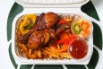 Overhead view of Haitian fried chicken in a to-go container with pikliz and other accoutrements.
