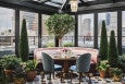 Interior of a greenhouse-style rooftop restaurant space with a decorative tree, a colorful tiled floor, and a pale pink round banquette.