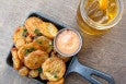 Golden-brown fried pickle rounds are served with thick orange dipping sauce in a small cast-iron pan, with beer on the side.