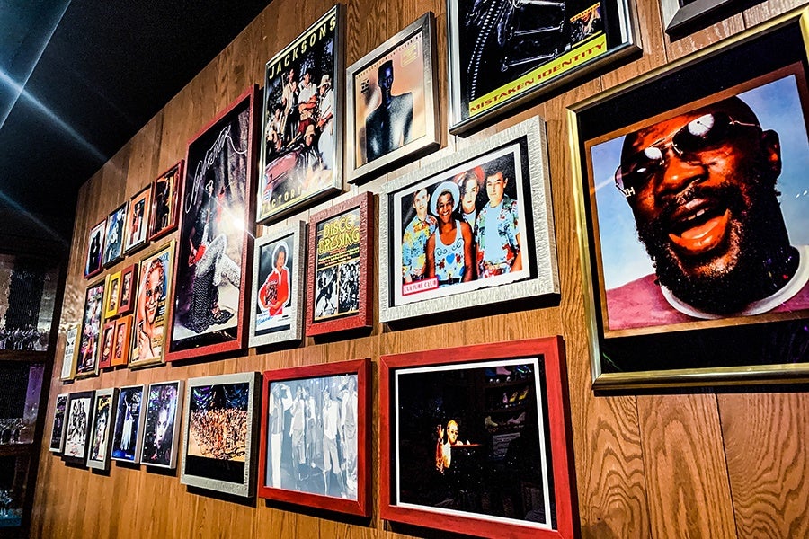 A wood-paneled wall is filled with photos of 1970s and 1980s musical groups in colorful frames.