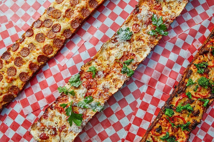 Three long, narrow pizzas are displayed on red-and-white-checkered paper.