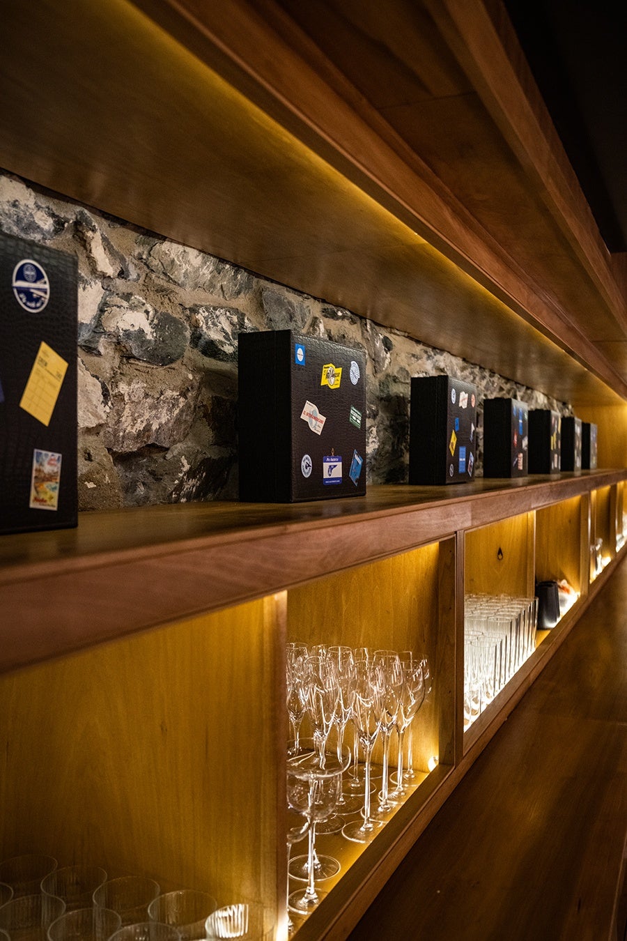 Suitcases with vintage travel stickers line wooden shelves on a stone wall.