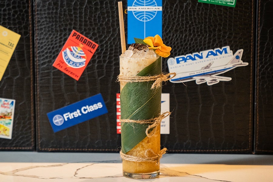 A banana leaf is wrapped around a glass of a tropical cocktail, garnished with a flower.