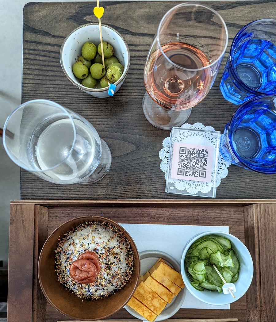 Overhead view of a table with sake glasses, olives, seasoned rice, Japanese-style egg omelet, and cucumbers.