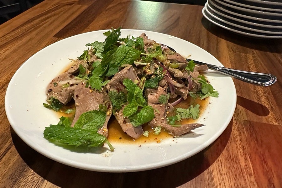 Thin slices of pork liver are garnished with fresh mint and other herbs on a white plate.