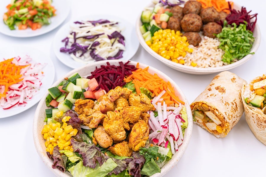 Two grain bowls and a wrap are filled with rice, paneer, chickpeas, and other ingredients.