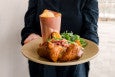A restaurant server in black clothing holds out a plate with a lobster-stuffed popover and side of greens.