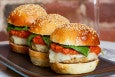 Three mini cheeseburgers topped with a tomato sauce and basil are displayed on a plate with a glass of rose to the side.