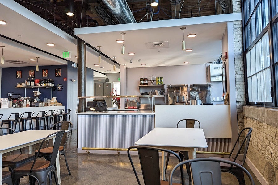 Interior of a small food hall, showing several counter-service dining spots with tables and chairs in a communal space.