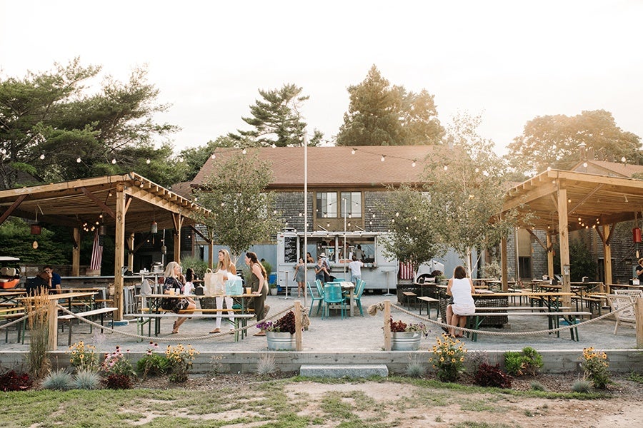 A sprawling outdoor restaurant patio features sections covered with wooden awnings and a food truck.