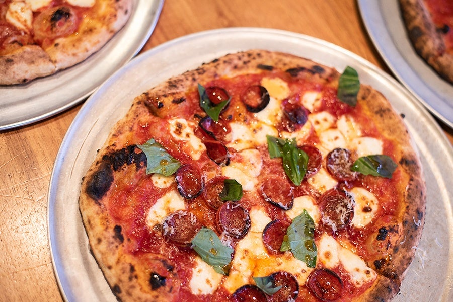 Closeup on a wood-fired pizza with pepperoni, mozzarella, and basil.
