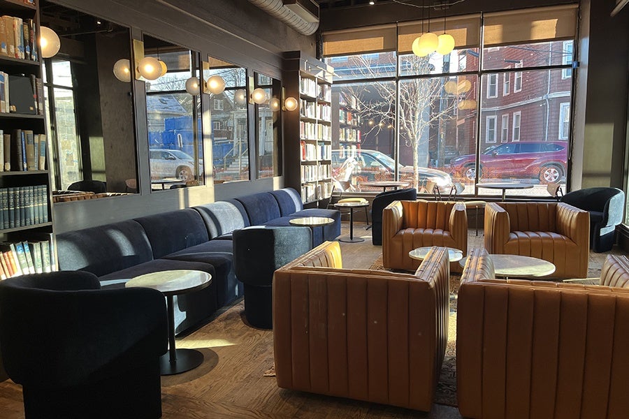 Interior of a restaurant and gathering space featuring lots of bookshelves and cozy yellow leather chairs and blue couches.