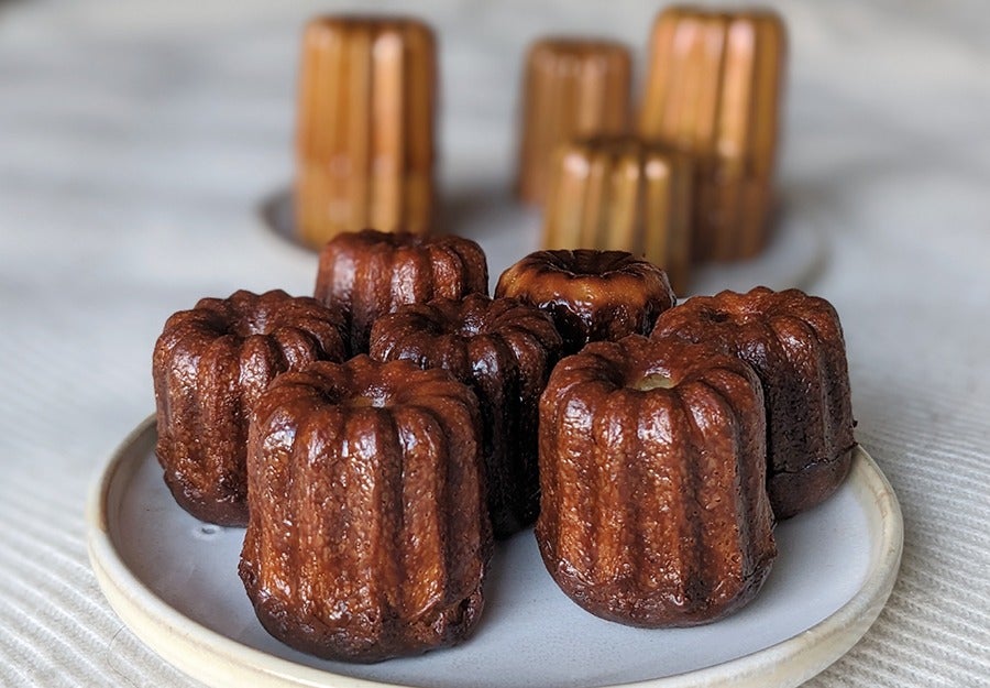 Shiny golden-brown canneles, little vertical pastries that look like mini, skinny bundt cakes.