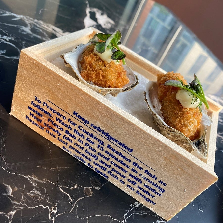 Two stuffed clams sit in a wooden box on a marble tabletop.
