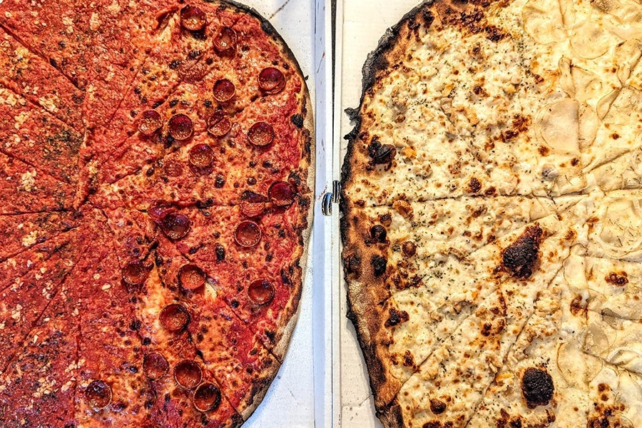 Overhead view of two thin-crust, charred, New Haven-style pizzas, one red and one white.