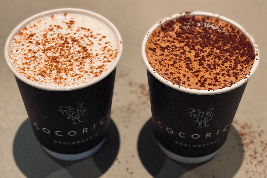 Two dark blue paper cups are full of hot chocolate—one white, one dark—each topped with cocoa powder.