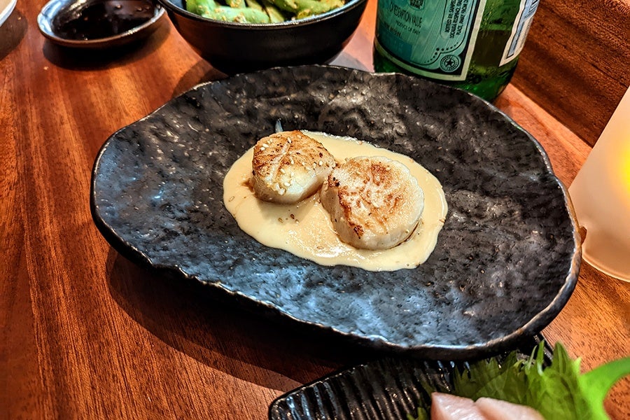 Two seared scallops sit in a pool of creamy sauce on a black plate.