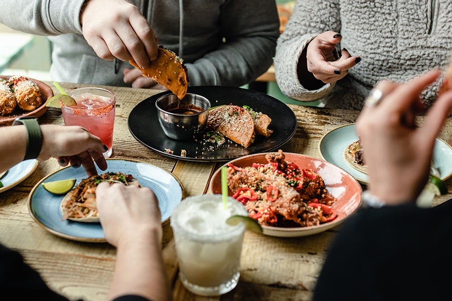 Several people are gathered around a table eating tacos and drinking margaritas.