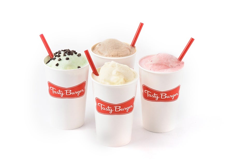 Four different flavors of milkshakes in white cups with red Tasty Burger branding sit on a plain white background.
