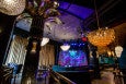 A jazz club features a variety of eye-catching light fixtures and gold palm leaves at the top of large black columns.