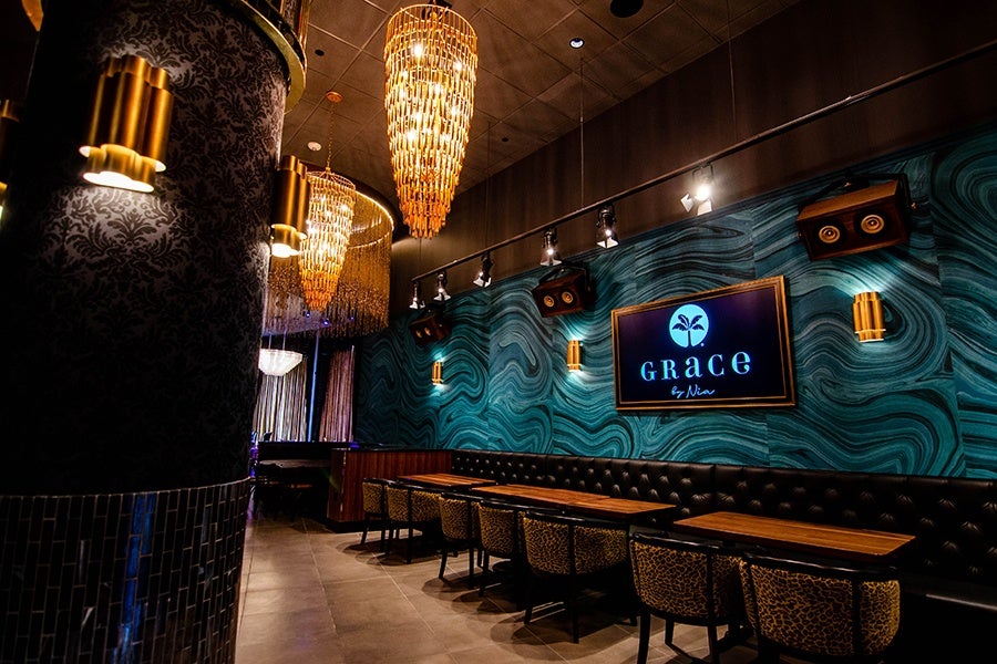 Leopard-print chairs and brown leather banquette seating span a dining area with teal wallpaper and large chandeliers.