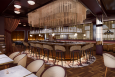 Rendering of a glamorous bar with dark brown wood accents and white marble tables.