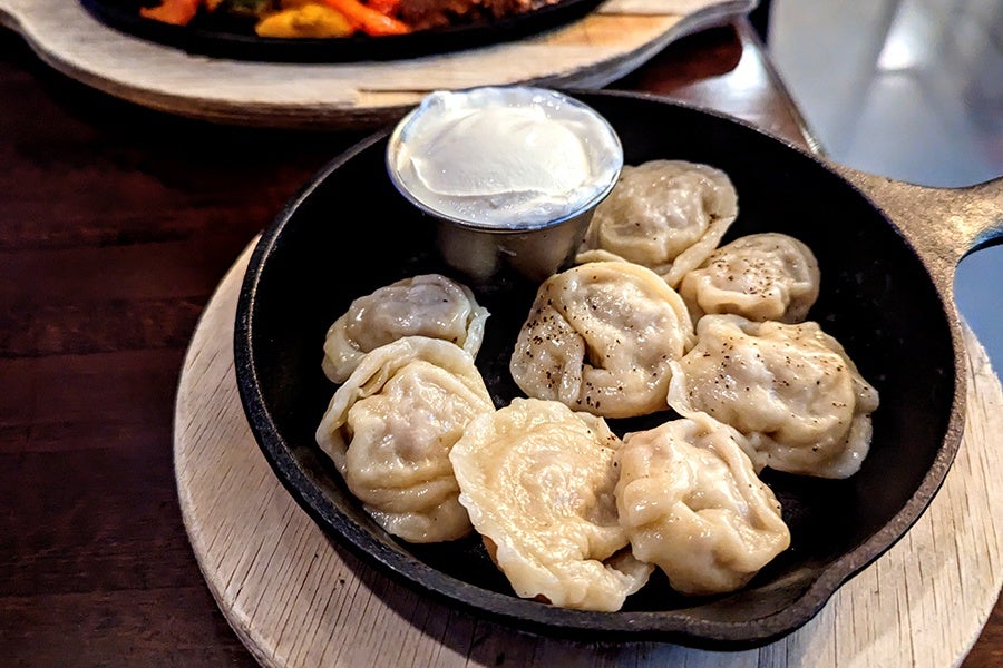 Plump dumplings with a side of thick sour cream sit in a round cast-iron pan on a wooden tray.
