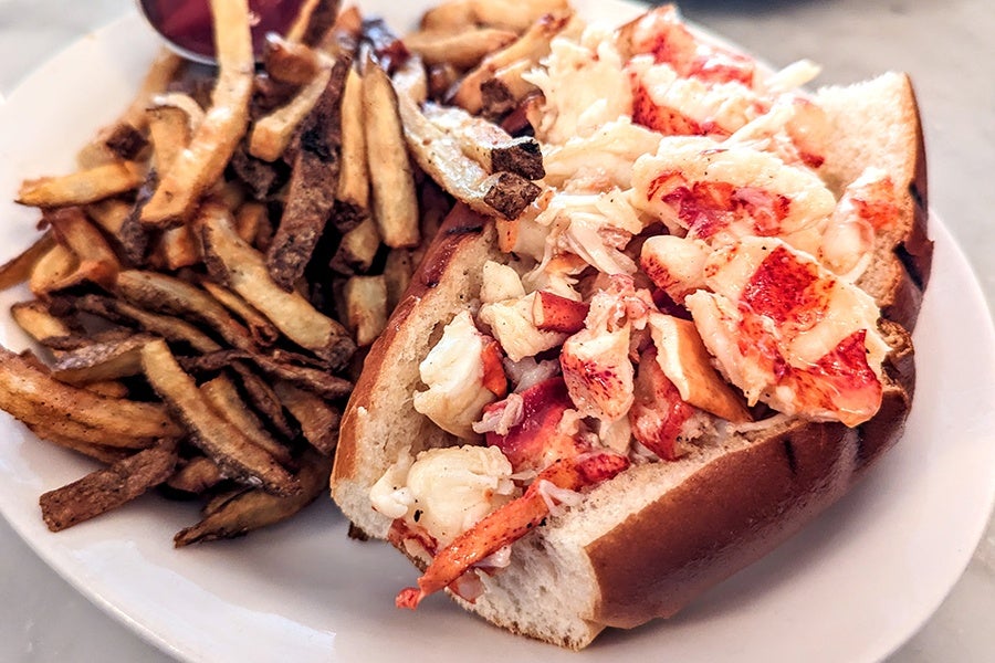 A lobster roll stuffed with ample meat has a side of fries.
