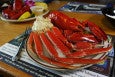 A shiny red whole lobster and crab legs sit on a plate on a wooden restaurant table.