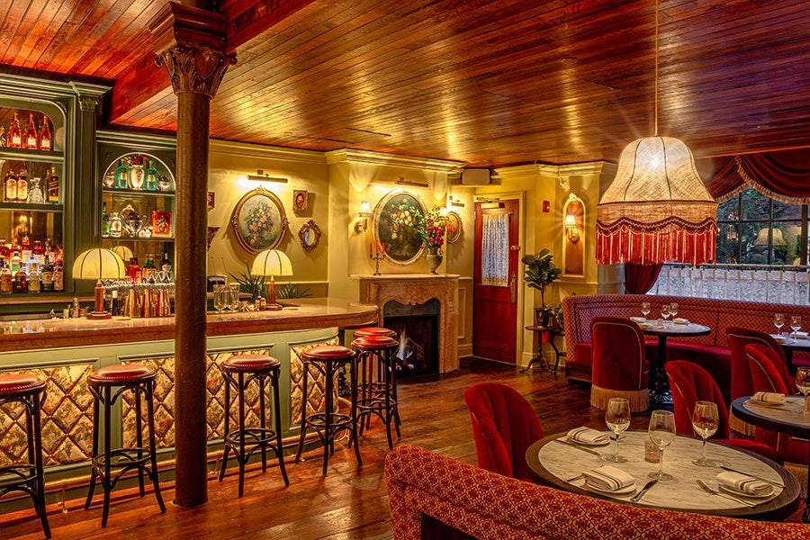 A room inside a restaurant is decorated in dark wood, red velvet, and pink marble.