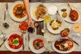 Overhead view of a white marble table covered with pasta, steak, and other Italian dishes.