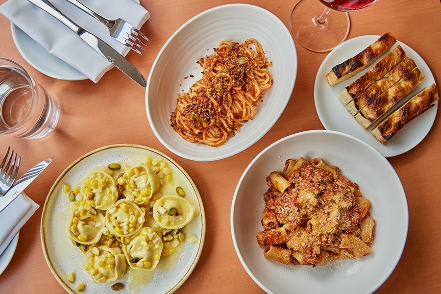 Overhead view of three different pastas on white plates and a side of focaccia-like fried dough.