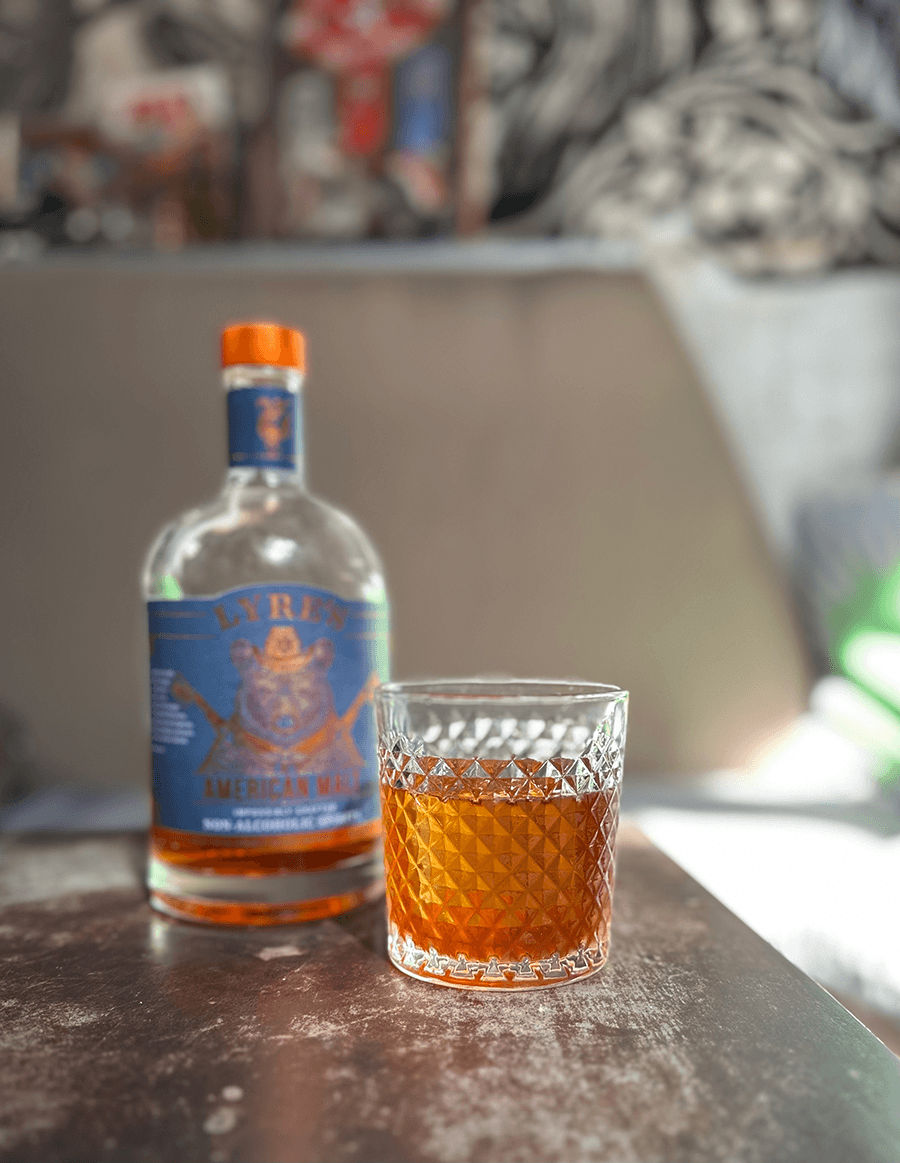 A brown cocktail sits next to a bottle of liquor.