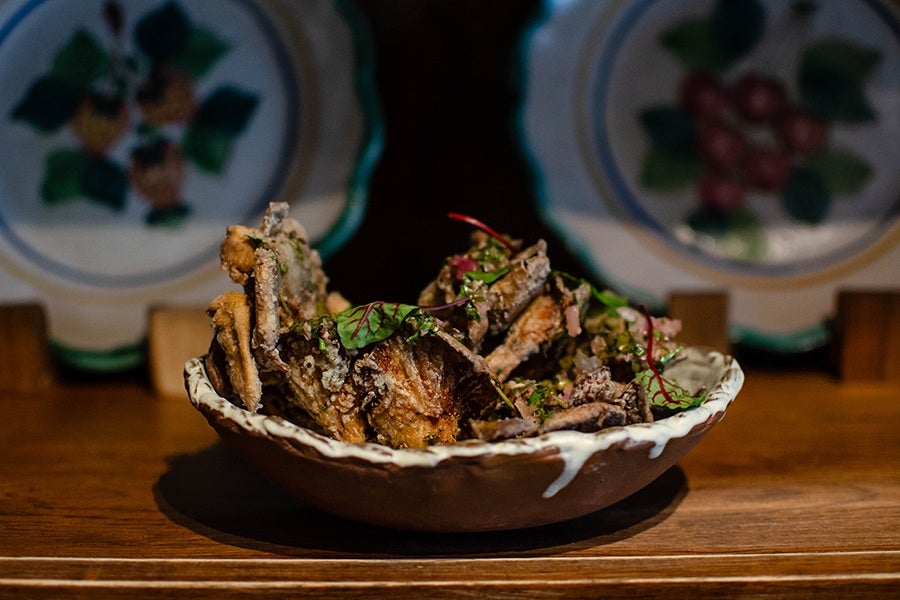 Large, crispy mushrooms in a brown bowl are topped with an herby green sauce and fresh herbs.