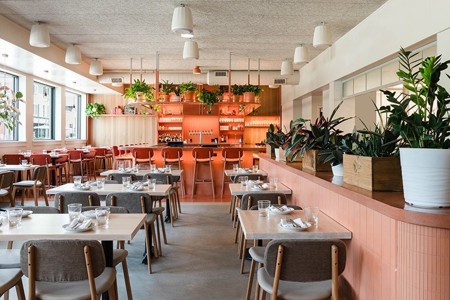 Restaurant interior photographed during the day, with lots of natural light. The space has white, grey, and peach tones and lots of plants.