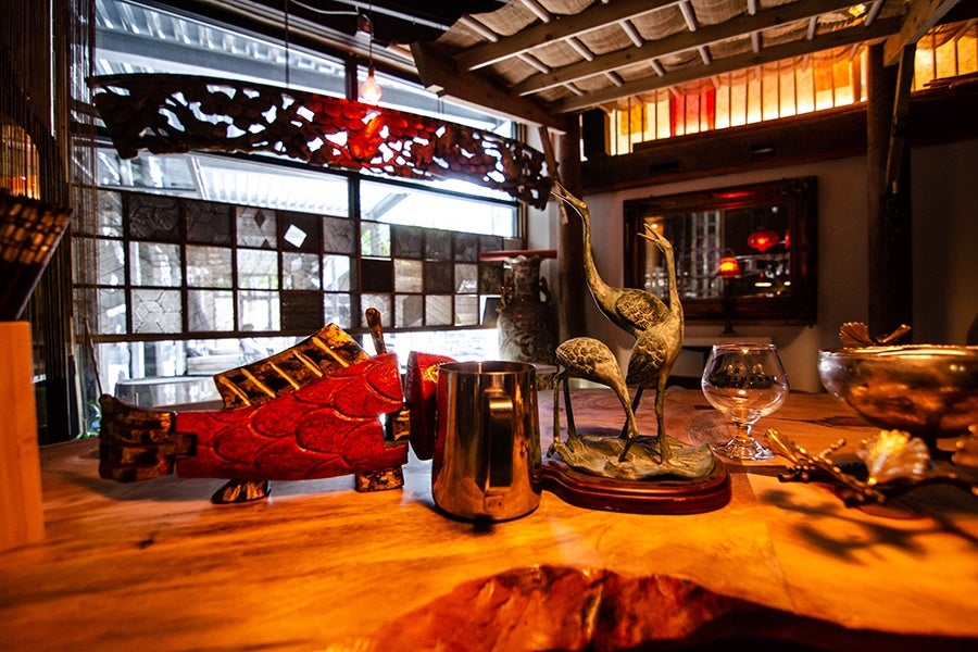 Decor details inside a small restaurant, including some vintage sculpture, a hanging wood carving, and a bamboo roof overhang.