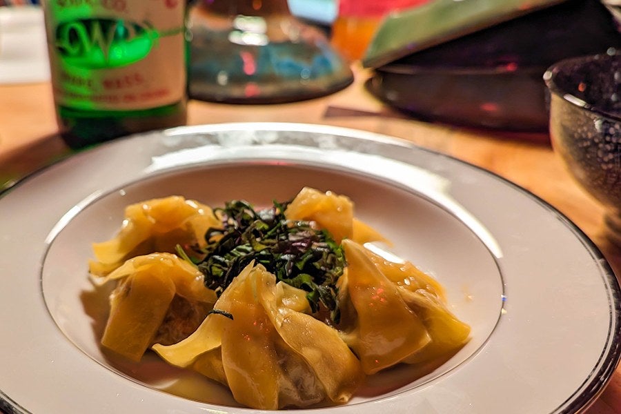 Small dumplings sit on a round plate, garnished with shreds of a dark green herb.