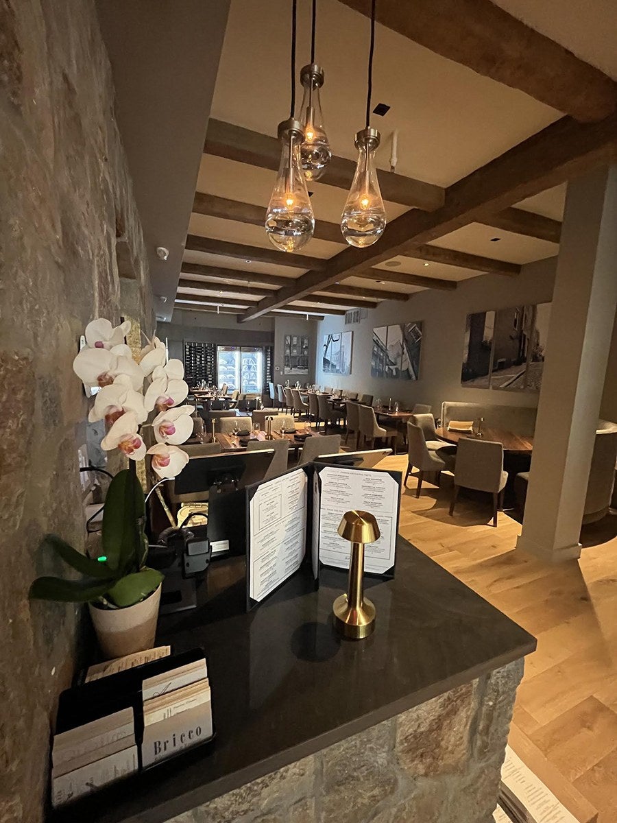 An empty restaurant features gray walls with large black-and-white photographs, wooden ceiling beams, and a bright, airy look.