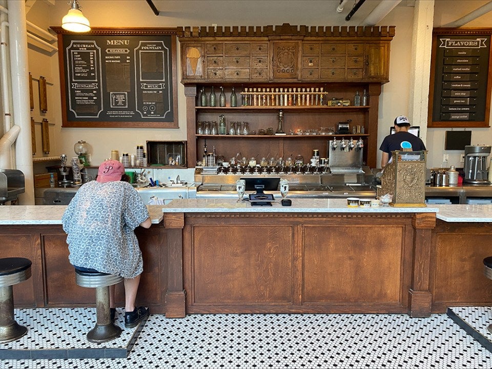 From behind, there's a person sitting at an ice cream counter with wooden structures.