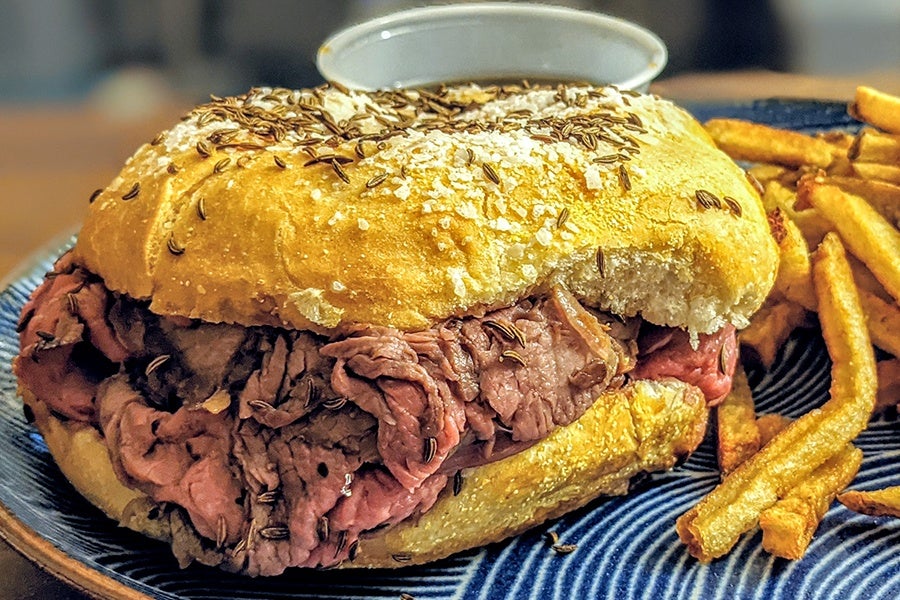 Close up on a roast beef sandwich with a roll covered in salt and caraway seeds.