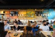 A somewhat casual restaurant with bright lighting and pops of yellow and blue is filled with diners.