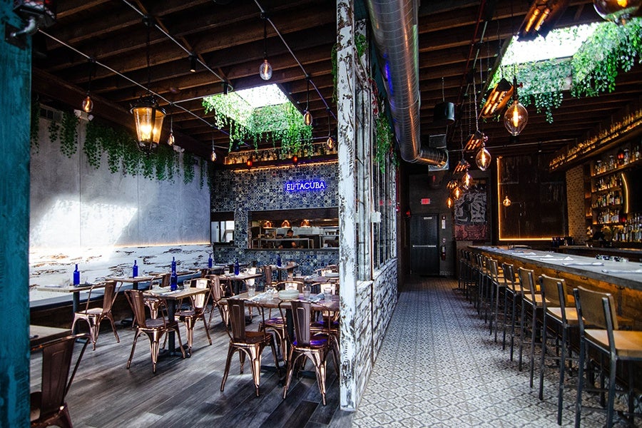 Interior of a Mexican restaurant featuring dining space and a bar. Two skylights have faux greenery hanging from the edges, and one wall is covered in blue and white Mexican tiling.