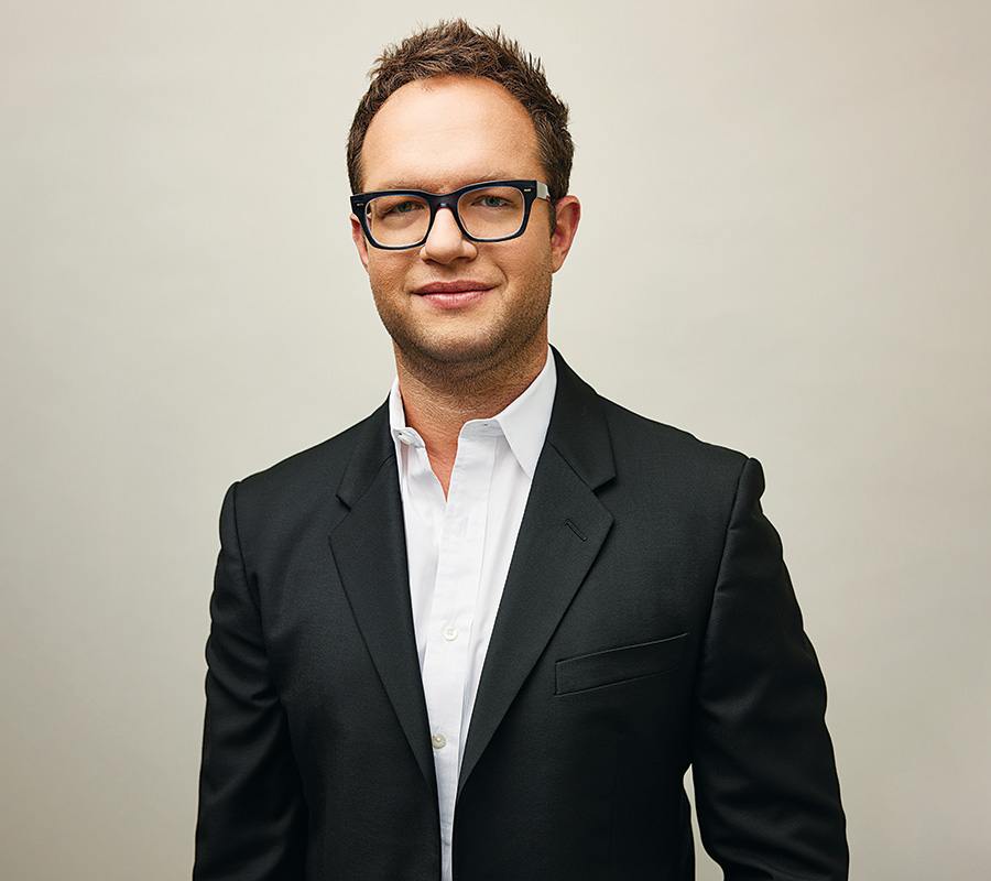 Sam Slater, a man with Elvis Costello eyeglasses, a white dress shirts and blazer with no tie.